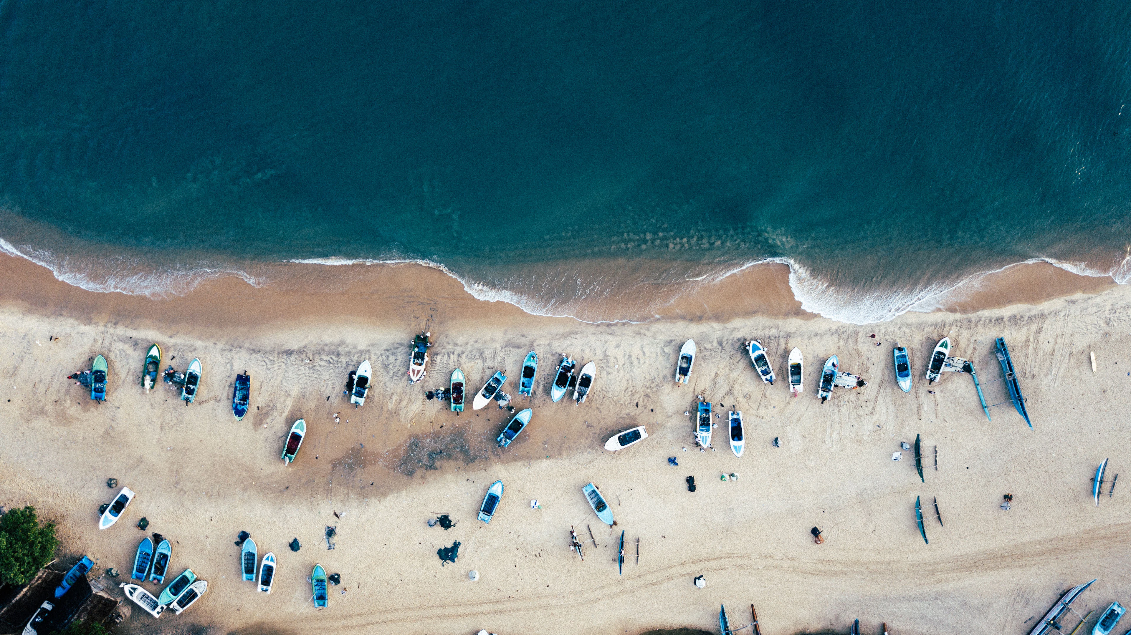 From above: fishing boats drawn up on the sand and people on the shore in the morning, Arugam Bay, Sri Lanka's east coast
