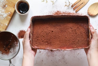 Close-up of rich, dark cocoa powder spilling from a rustic wooden bowl.