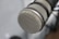 A close-up of a professional microphone with a metal mesh grille, highlighting the intricate pattern of the mesh. The microphone is positioned at an angle with a blurred background, providing a sense of depth.