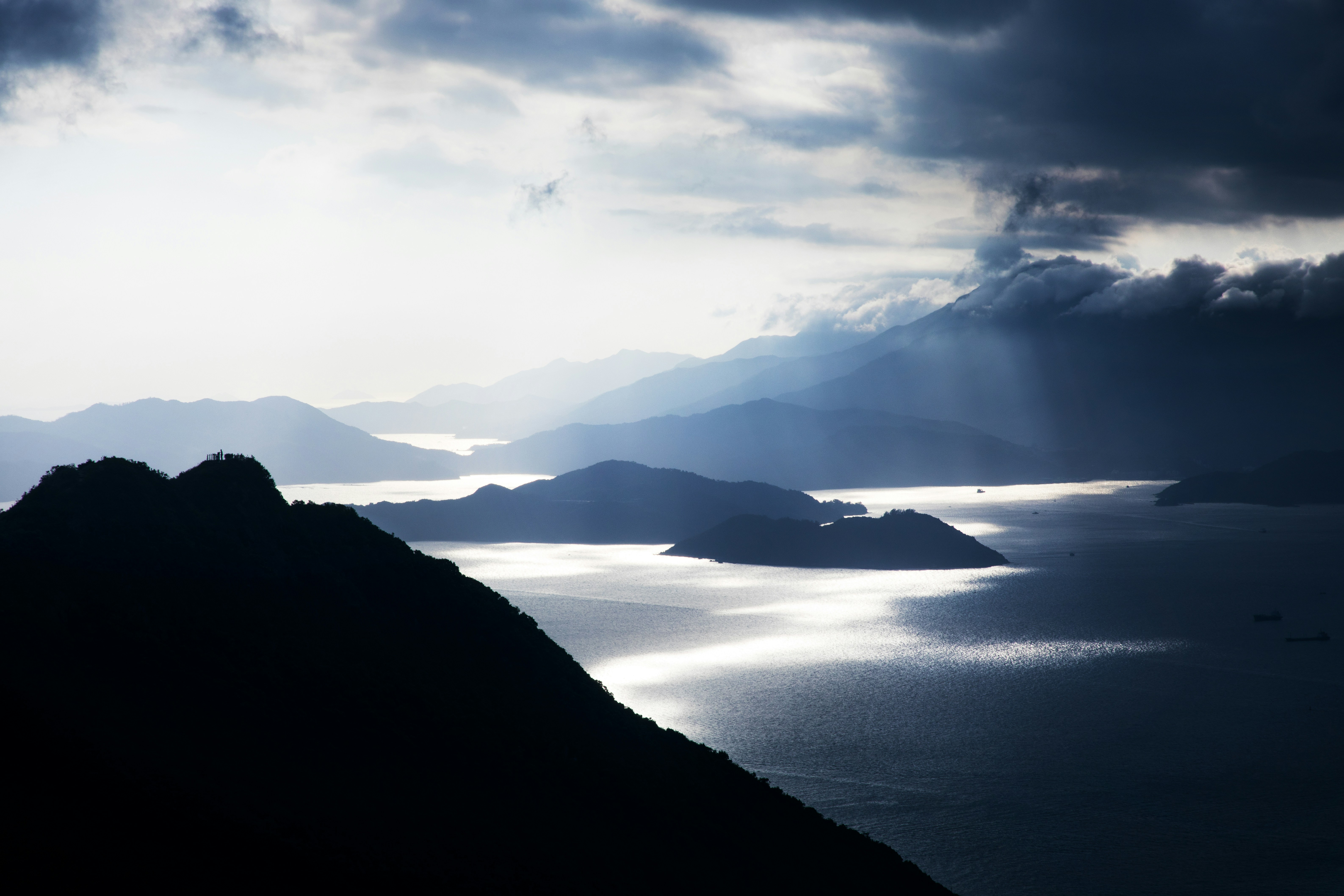 A landscape photo of clouds covering half of a body of water, casting dark shadows, in contrast with the sunlit other half.