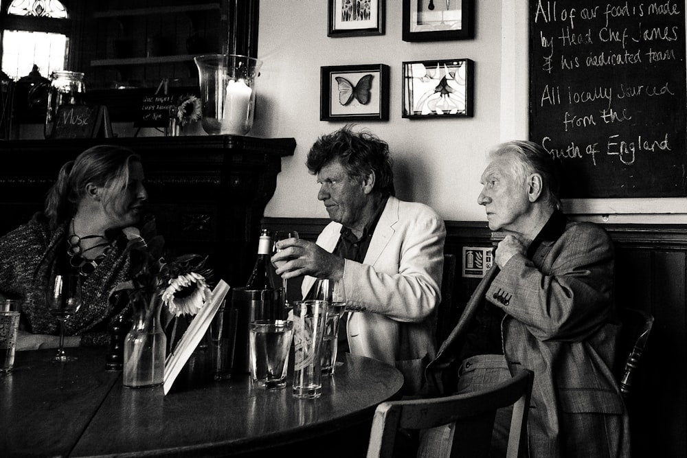 Foto en escala de grises de tres hombres sentados al lado de la mesa