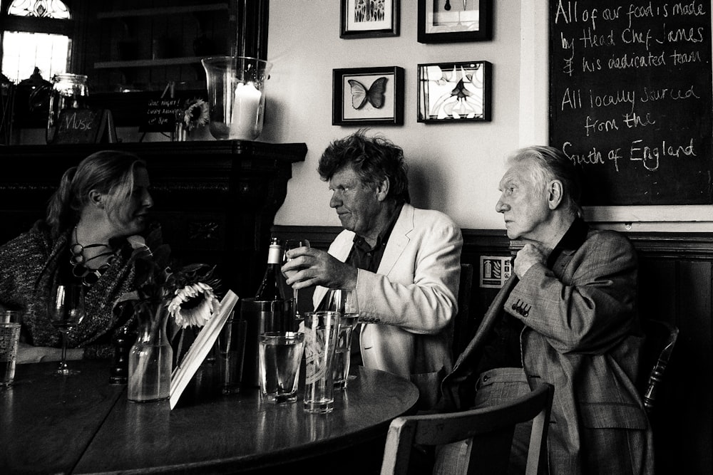 grayscale photo of three man sitting beside table