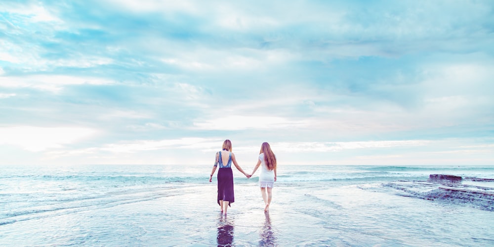 two women walking on shoreline holding hands