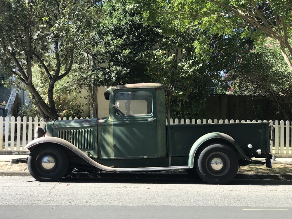 vintage green vehicle near white fence during daytime