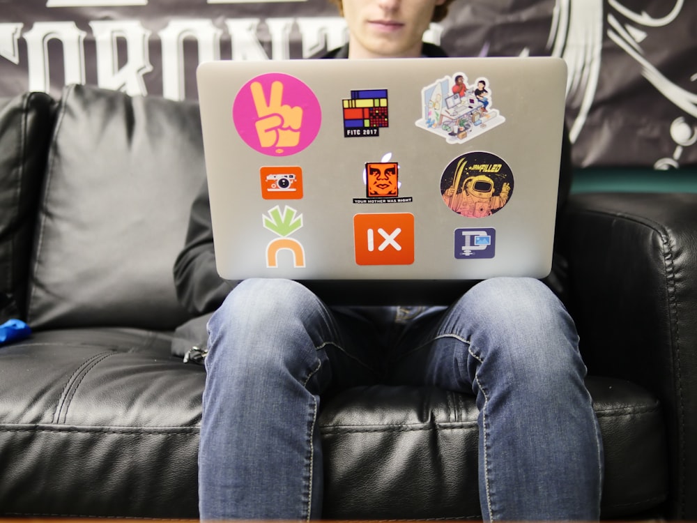 hombre usando MacBook plateado sentado en un sofá de cuero negro