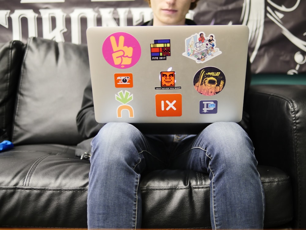 man using silver MacBook sitting on black leather sofa