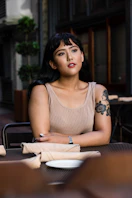 woman wearing brown tank top leaning on black wooden table with white ceramic plate