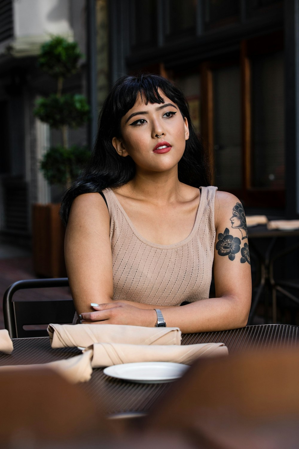 woman wearing brown tank top leaning on black wooden table with white ceramic plate