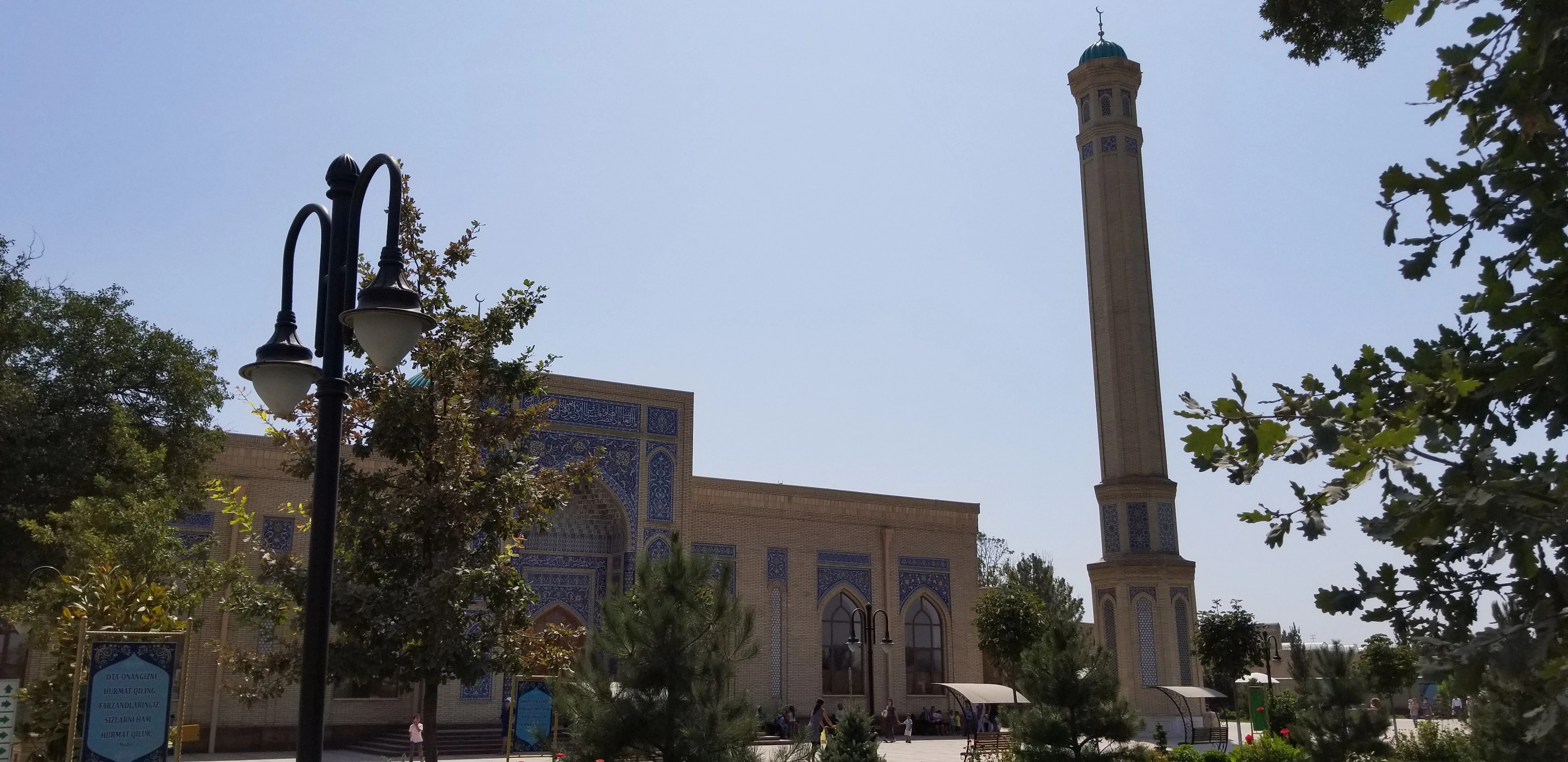 The blue-tiled facade and tall minaret of the Zangiota mosque complex, framed by trees, in the Tashkent region of Uzbekistan