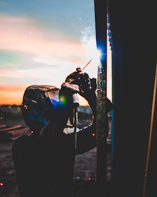 Workers welding steel plates during a ship repair at dusk with sparks flying.