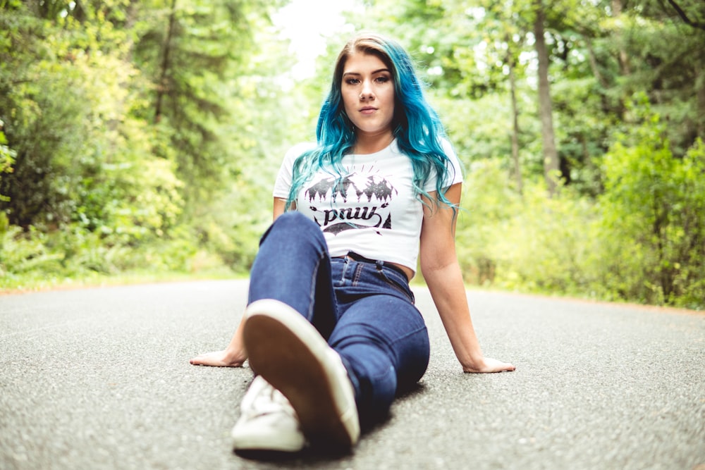 woman in white t-shirt and blue denim jeans sitting on road during daytime