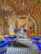 An artistic and vibrant café interior with blue chairs featuring patterned fabric, wooden tables, and decorative ceiling fixtures. The room features a series of arches and a checkered tiled floor, creating a cozy but stylish atmosphere.