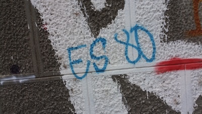 Graffiti on a textured wall featuring the letters 'ES 80' in blue, with white and red paint patches.
