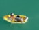 A small yellow boat on teal water with two people handling fishing nets while checking a bucket of fish. An outboard motor is attached at the back of the boat.