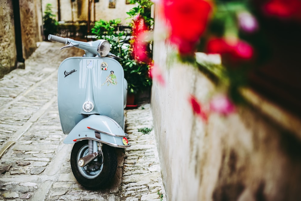 selective focus photo of blue motor scooter beside concrete wall