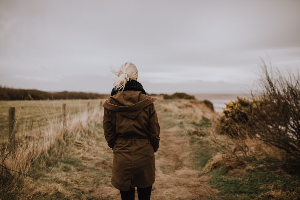 woman in brown coat walking on brown grass