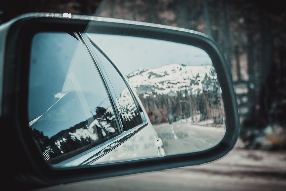 Blick auf die schneebedeckten Berge aus dem rechten Seitenspiegel des grauen Fahrzeugs