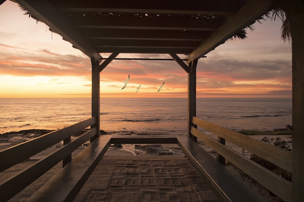 Cabana de madeira marrom ao lado da costa durante o pôr do sol laranja