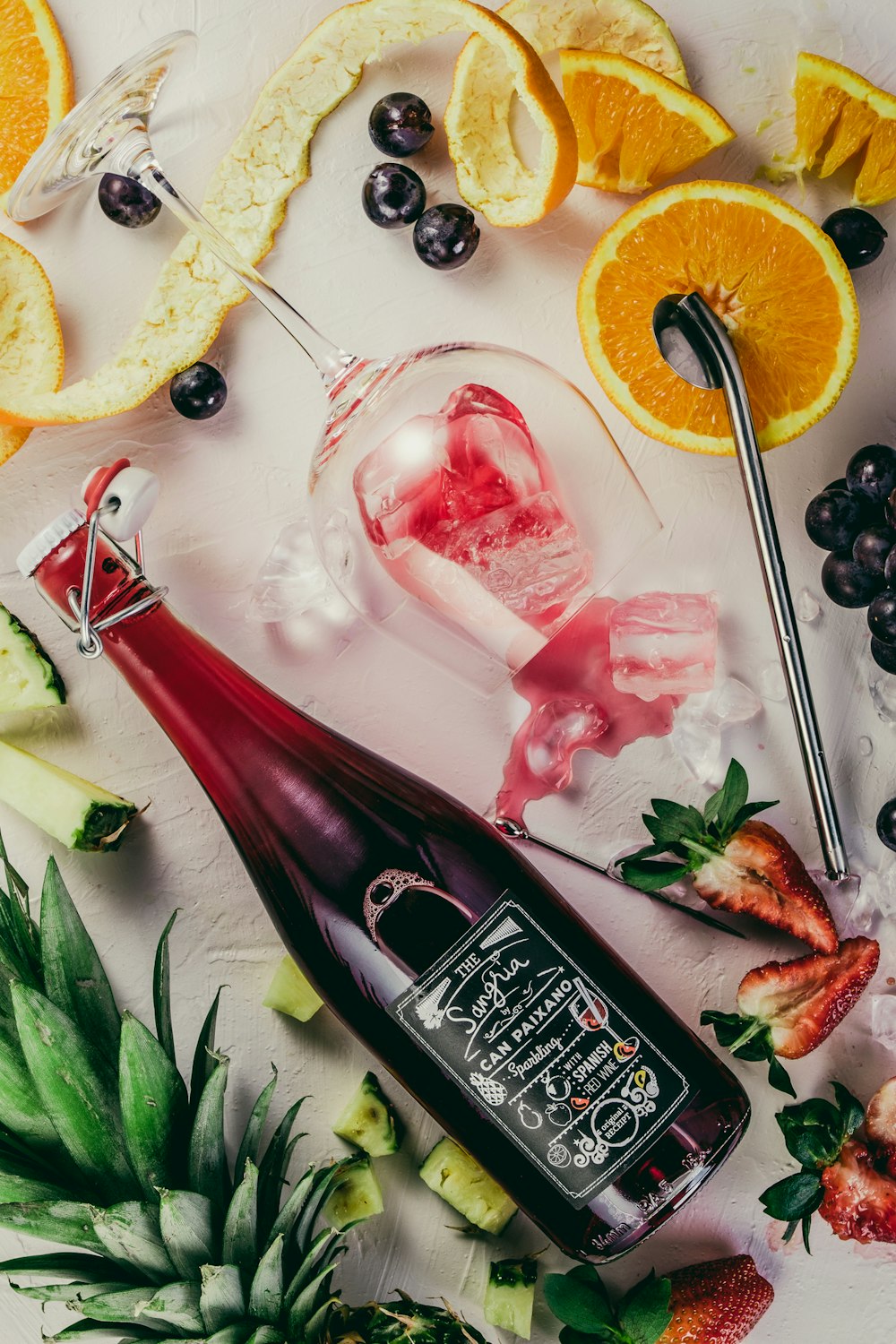 flat-lay photograph of sliced fruits, swing top bottle, and wine glass