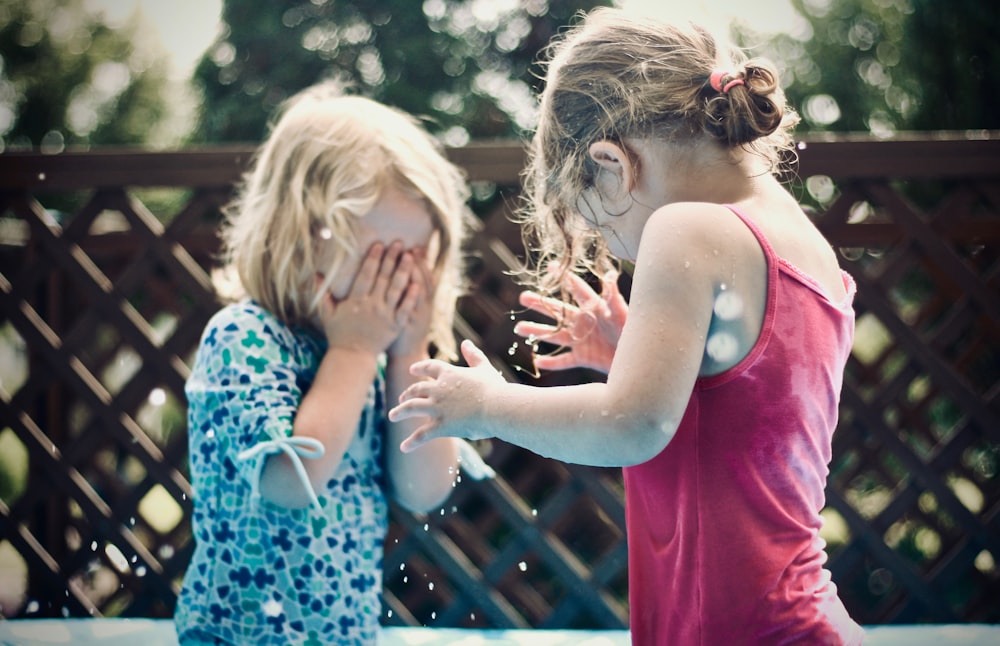 Due bambini che giocano con l'acqua durante la fotografia diurna a fuoco superficiale