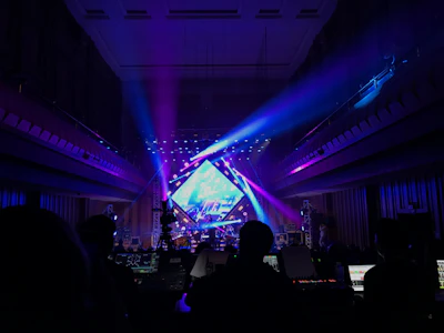 A dramatic wide shot of a live concert stage illuminated with red and dark gray lighting, capturing the energy and technical setup.