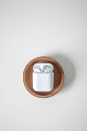 Wireless earphones in a charging case placed on a round, textured cork surface against a white background.