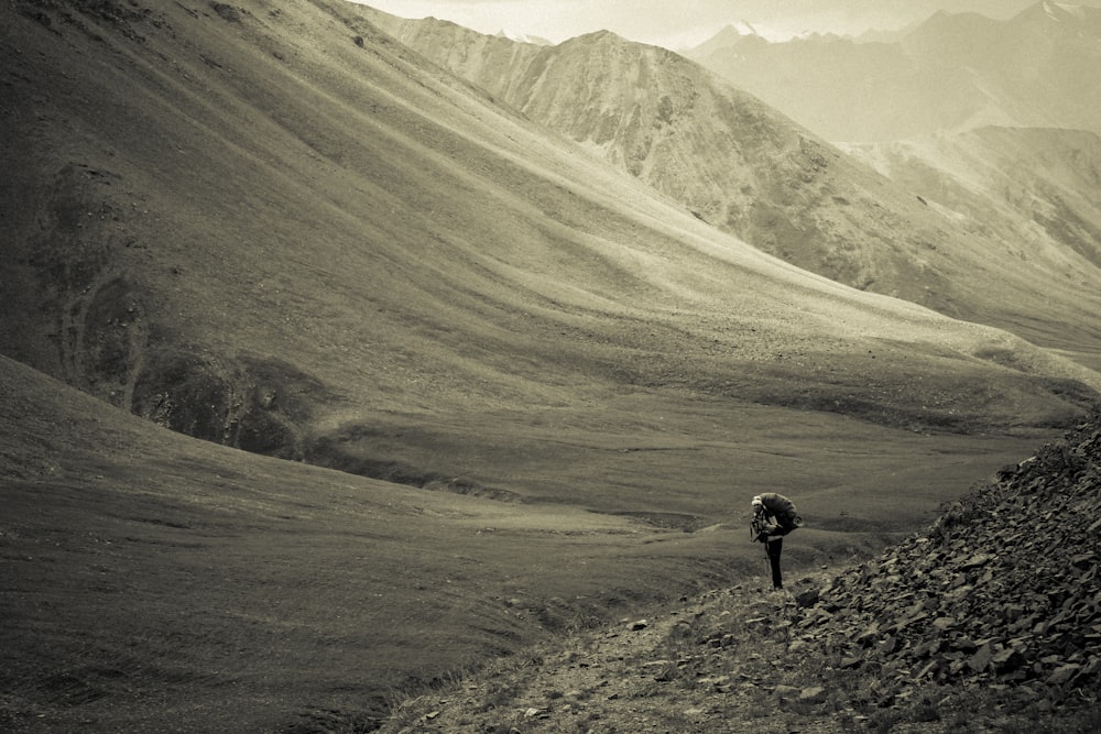 grayscale photo of person walking on mountain feet during daytime