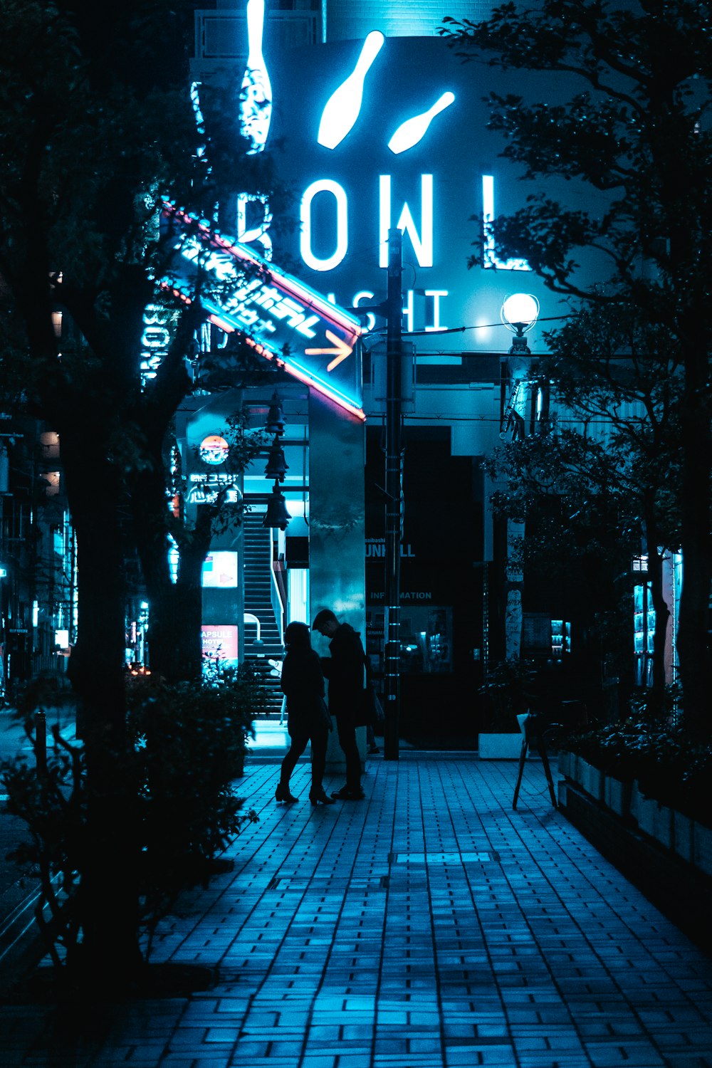 a couple of people walking down a sidewalk at night