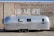 An aluminum travel trailer is parked against a brick wall. The wall features a mural with large, bold white letters that read 'YOU ARE HERE.' The trailer's shiny surface reflects its surroundings.