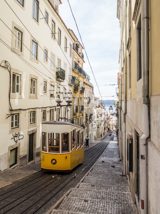 yellow and white bus in the middle of white buildings during daytime in Elevador da Bica Portugal