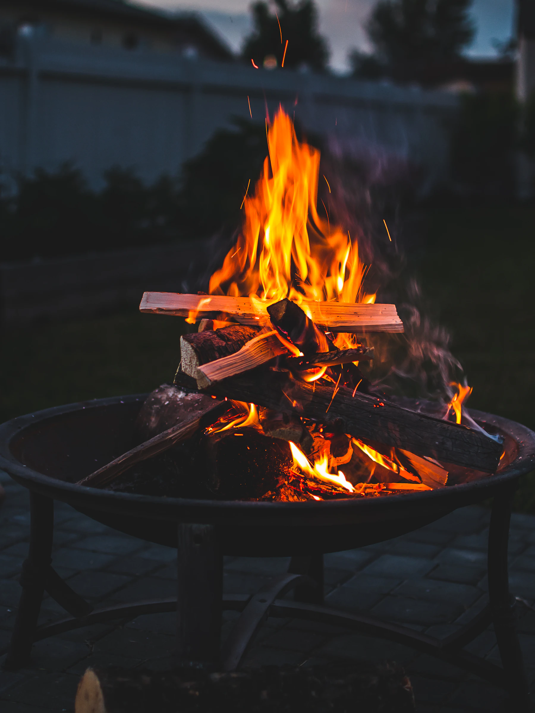 A steel fire bowl burning on a stone terrace at sunset with open water beyond
