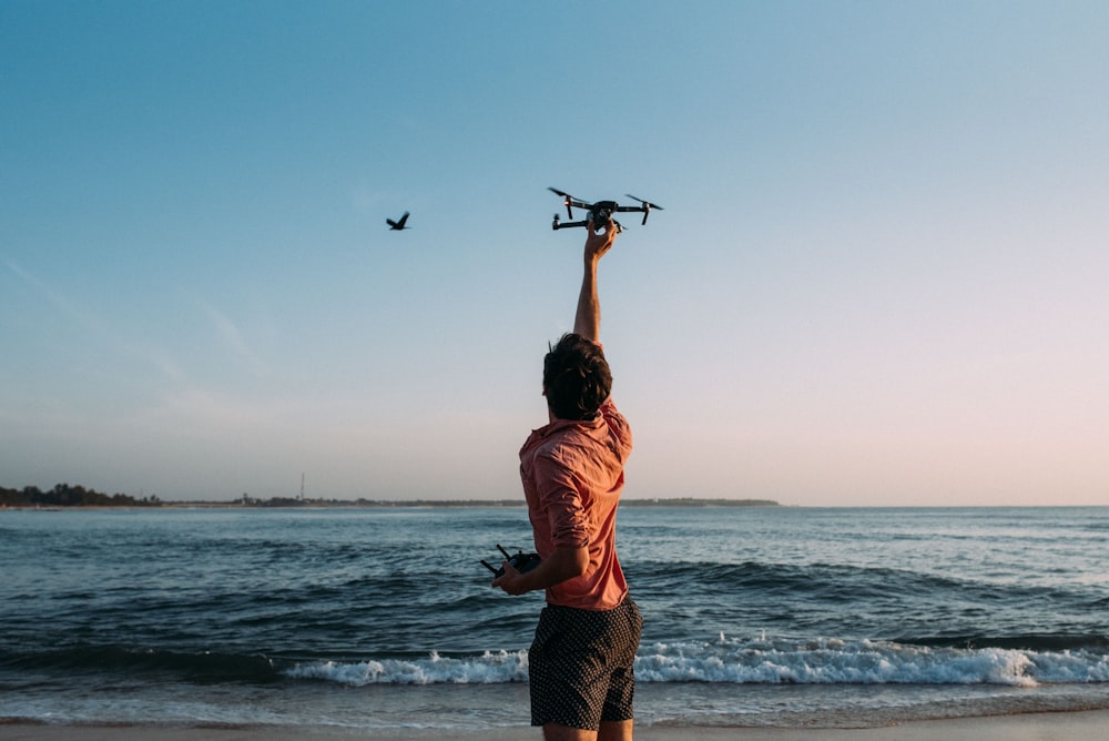 Hombre sosteniendo un dron cerca del océano