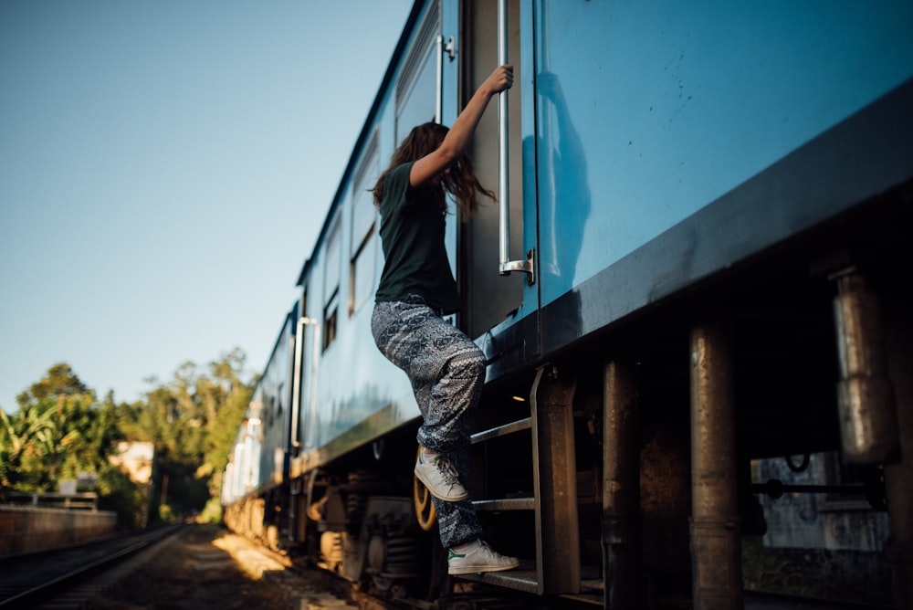 woman in black top and gray pants holding on blue train