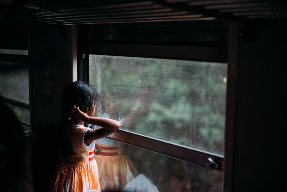 chica con vestido naranja sin mangas mirando a la ventana