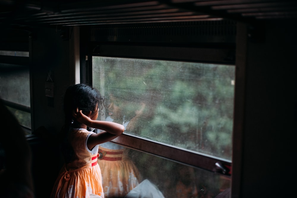 girl in orange sleeveless dress looking at the window