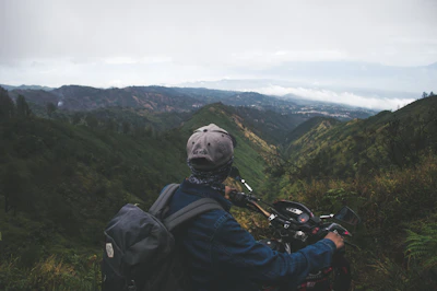 A happy traveler wearing a helmet, riding a motorbike past lush green hills.