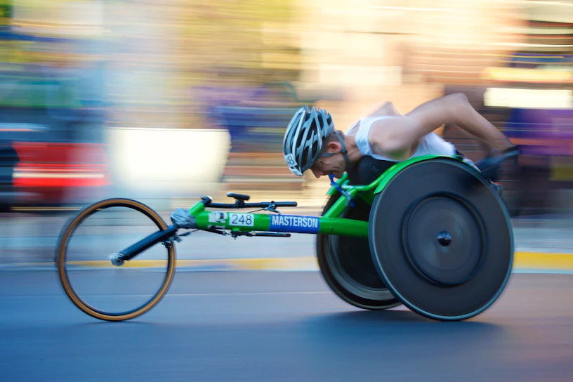 A focused para triathlete in a racing wheelchair powering through a sunny track.