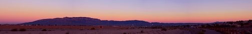 A panoramic view of a desert landscape with faint outlines of structures blending into the horizon.
