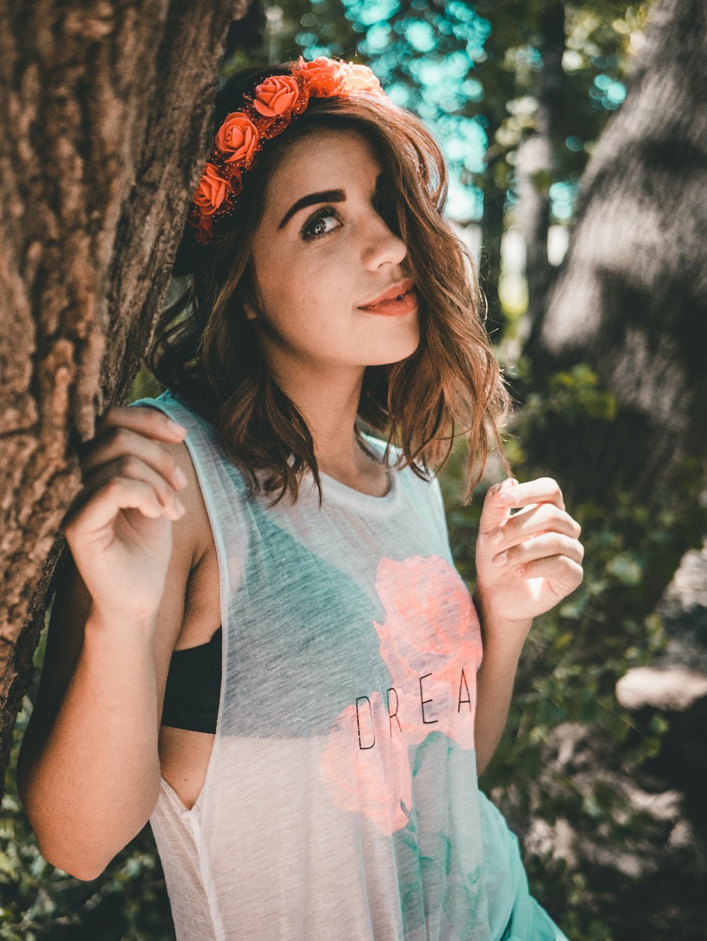 woman wearing black bra and green see-through tank top leaning on brown bark tree during daytime