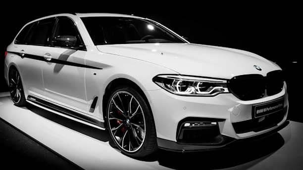 A sleek, white, luxury BMW car with sporty design elements, highlighted by black trim and aerodynamic contours. The vehicle is captured in a well-lit setting, emphasizing its glossy finish and intricate headlight design.