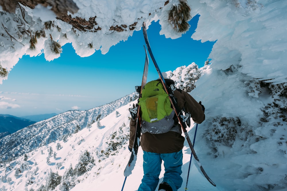 person carrying green backpack standing on snow-covered mountain during daytime