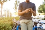 man holding smartphone leaning on bicycle during daytime