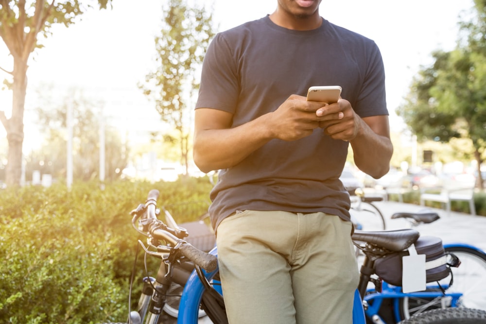 Mann mit Smartphone, das sich tagsüber auf ein Fahrrad stützt