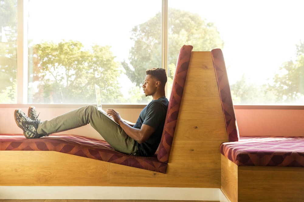 man sitting on red cushion beside window