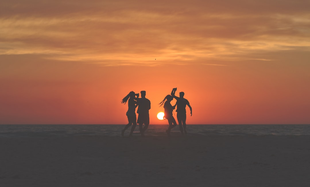 silhouette photo of four people dancing on sands near shoreline