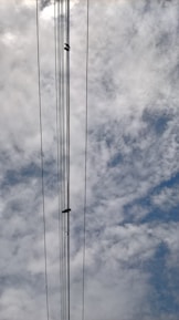 Several power lines stretch vertically against a backdrop of a cloudy sky. The clouds vary in density and the sky appears partly cloudy with hints of blue visible through the gaps.