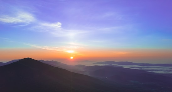 A vibrant photo of a happy traveler looking out over a scenic mountain vista at sunrise.