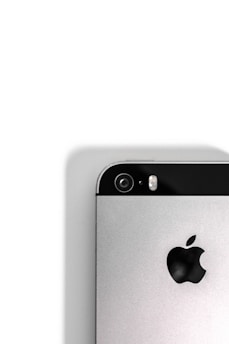 A close-up view of the back of a silver smartphone, featuring a camera lens, flash, and the iconic apple logo. The upper portion of the phone contains a black strip that houses the camera and flash components, while the rest of the body is metallic.