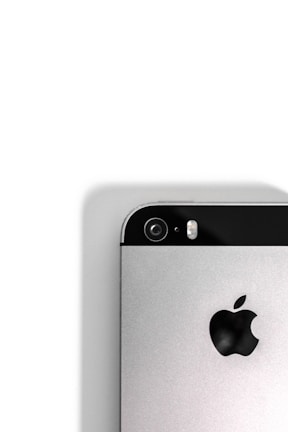 A close-up view of the back of a silver smartphone, featuring a camera lens, flash, and the iconic apple logo. The upper portion of the phone contains a black strip that houses the camera and flash components, while the rest of the body is metallic.