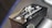 A close-up of a motorcycle part with embossed text and symbols. The text 'Hayabusa' is prominently featured alongside a stylized Japanese character. The part has a metallic, angular design with a black finish and highlights visible on its surface.